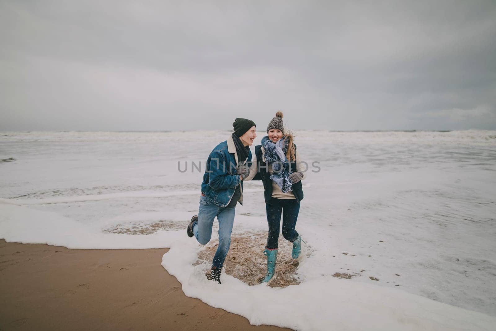 A young couple laugh and paddle in the sea on a winter beach.