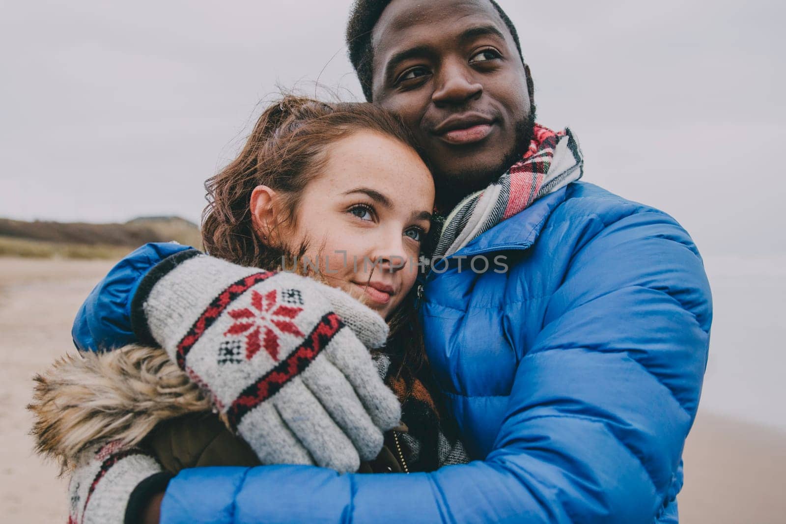 A young couple hug and look into the distance on a winter beach.