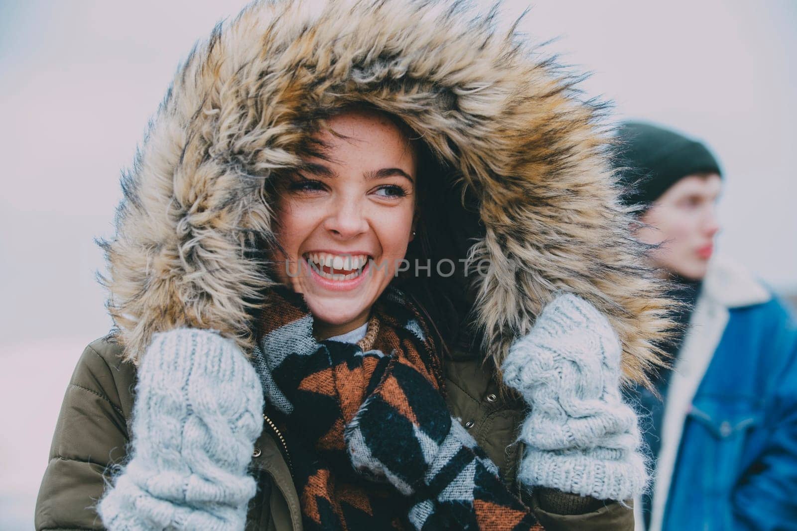 A woman laughing on a winter beach with an out of focus male in the background.