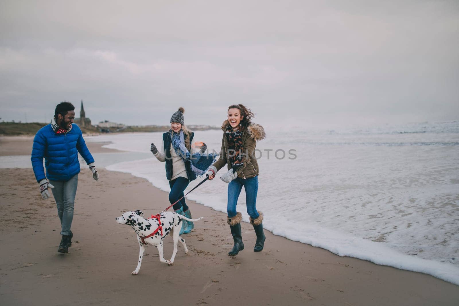 Three friends walk a dog along Tynemouth beach in winter.