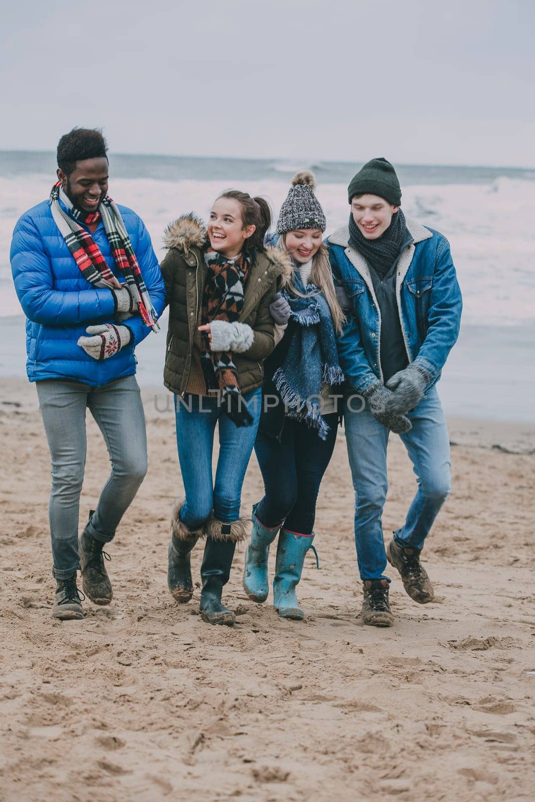 A group of friends talking and laughing whilst walking along a winter beach.