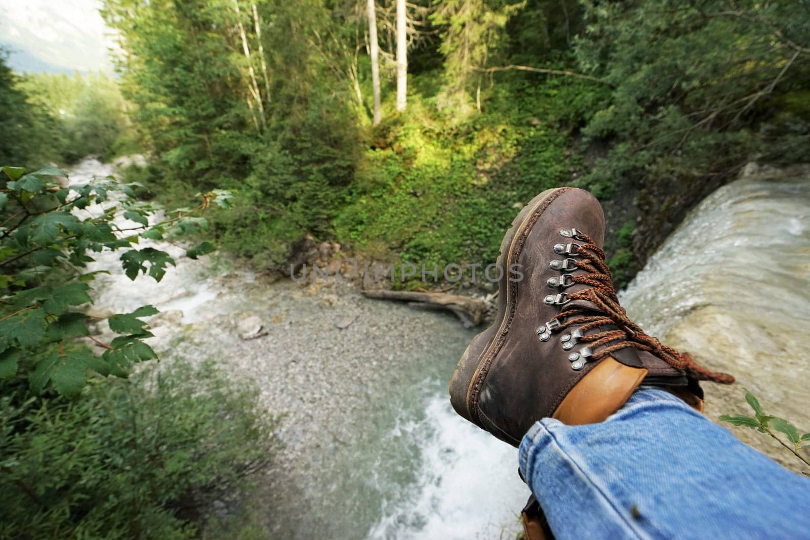 Young man at a waterfall,you can see the mountain boots