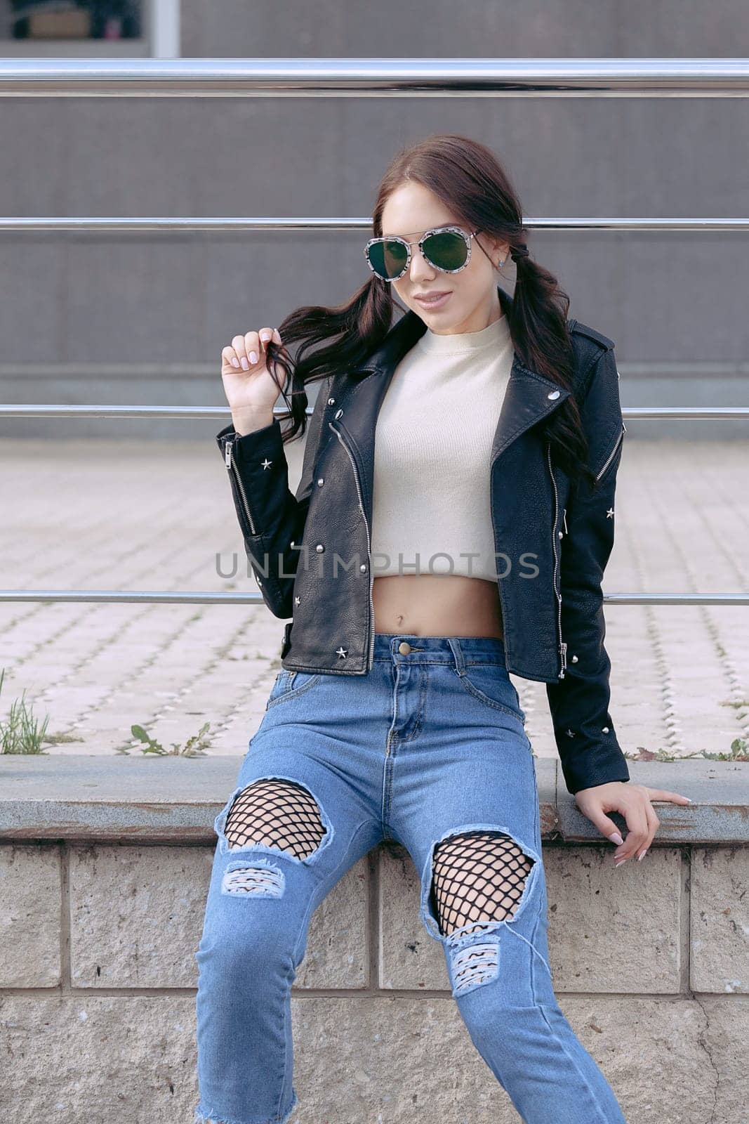 fashionable young woman in rock style clothes, black leather jacket, blue jeans, tights in a grid under battered jeans.