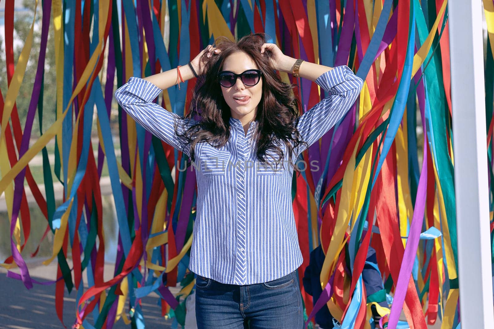 portrait of a young beautiful woman in dark glasses on a summer sunny day against the background of colorful ribbons in the park on vacation.
