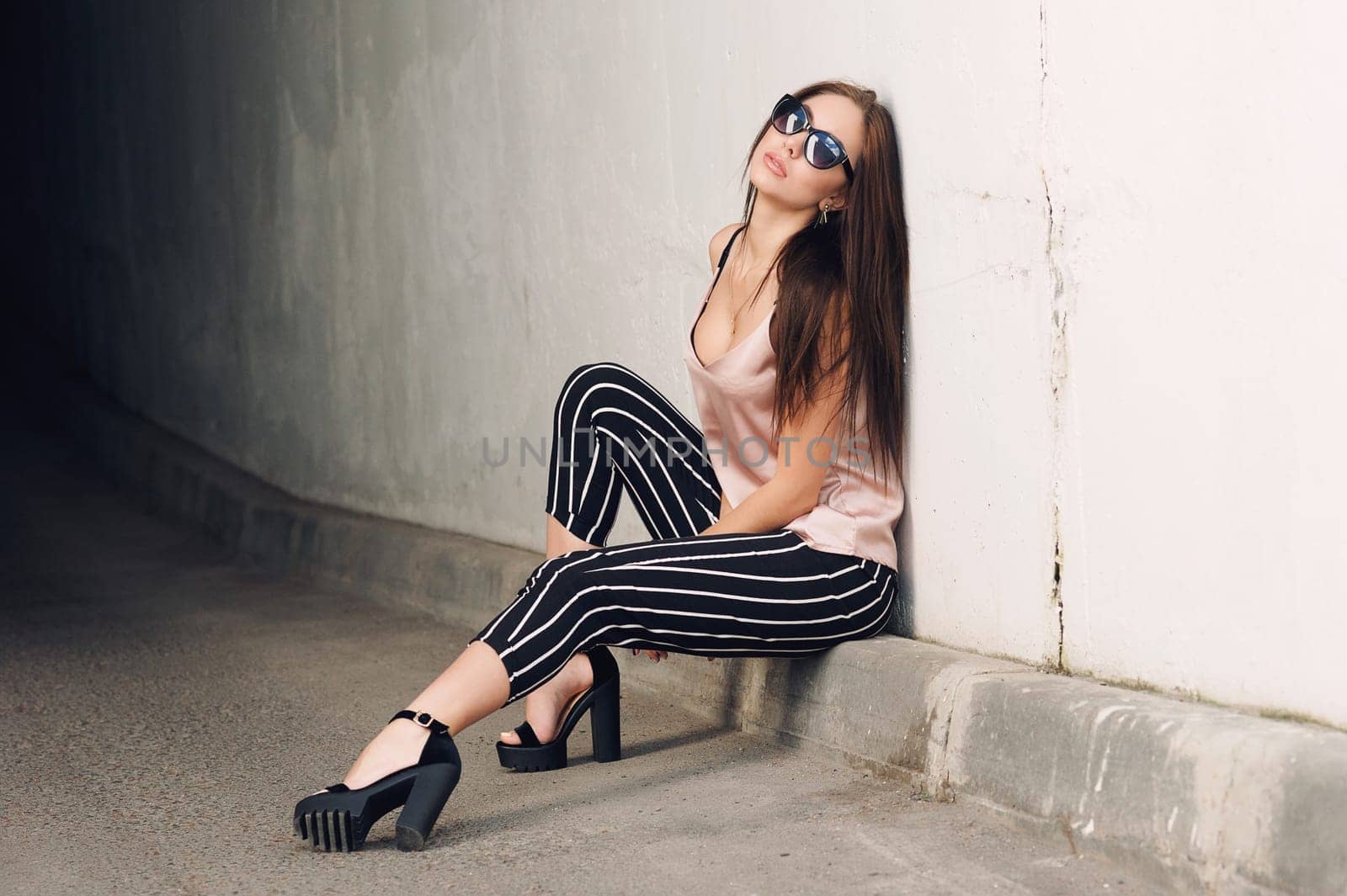 Outdoor portrait of a young beautiful fashionable happy lady, wearing sunglasses, in a wooden frame, creating a city on the street. The model wears stylish clothes. The girl is looking up, the hair is developing in the wind. Women's fashion. Urban way of life.