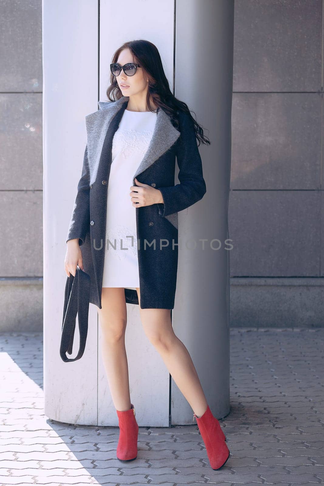 Outdoor portrait of a young beautiful fashionable woman, outdoors. A model dressed in a stylish gray coat, sunglasses. The concept of women's fashion, urban lifestyle.