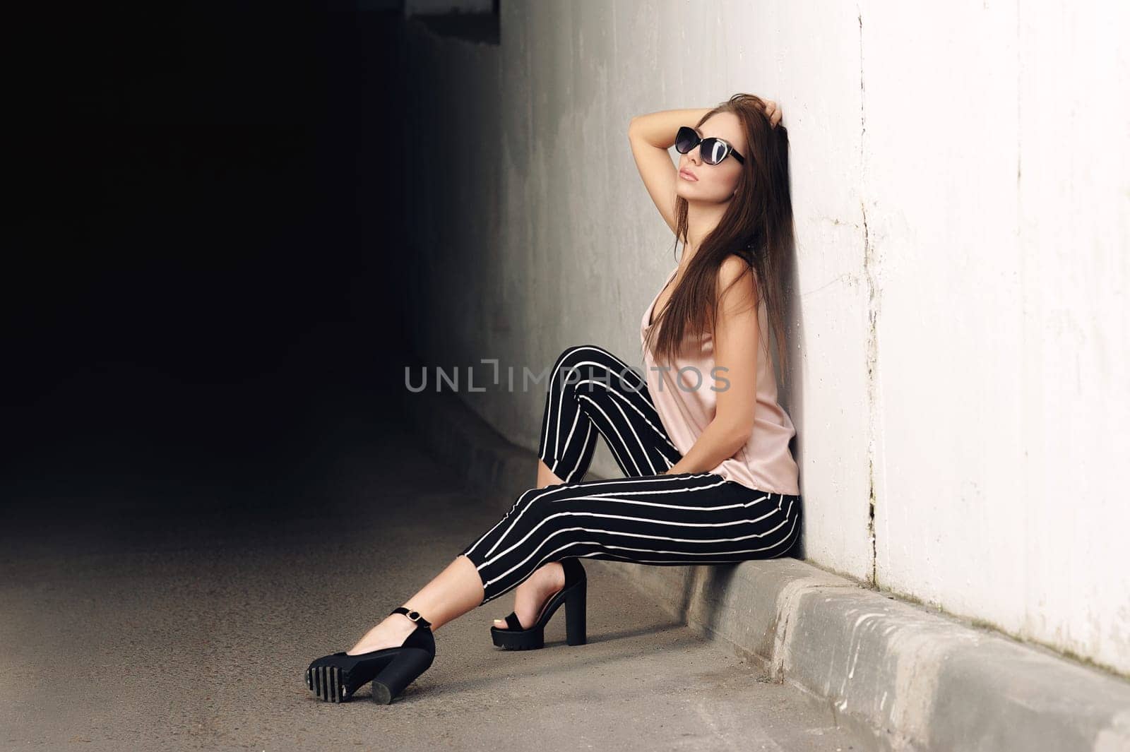 Outdoor portrait of a young beautiful fashionable happy lady, wearing sunglasses, in a wooden frame, creating a city on the street. The model wears stylish clothes. The girl is looking up, the hair is developing in the wind. Women's fashion. Urban way of life.