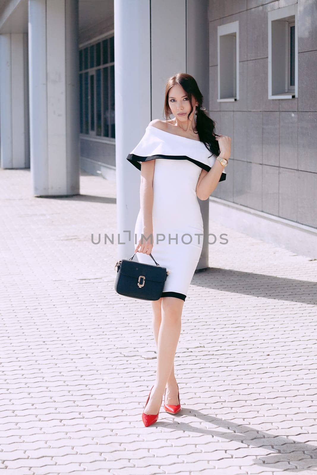 Young beautiful stylish girl in white dress and black bag. walk and pose outdoors. fashion style, shopping. The concept of women's fashion, urban lifestyle