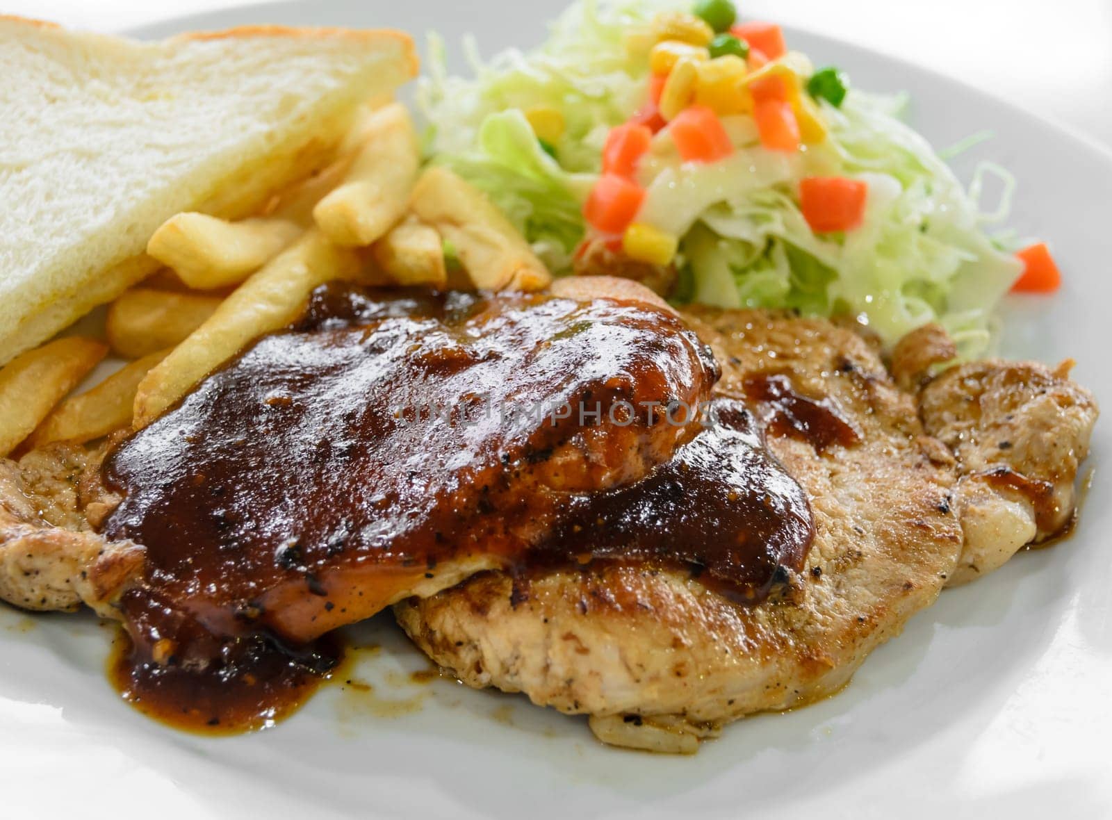 Grilled pork steak fillet with black pepper sauce, vegetable salad, bread and french fries on white plate