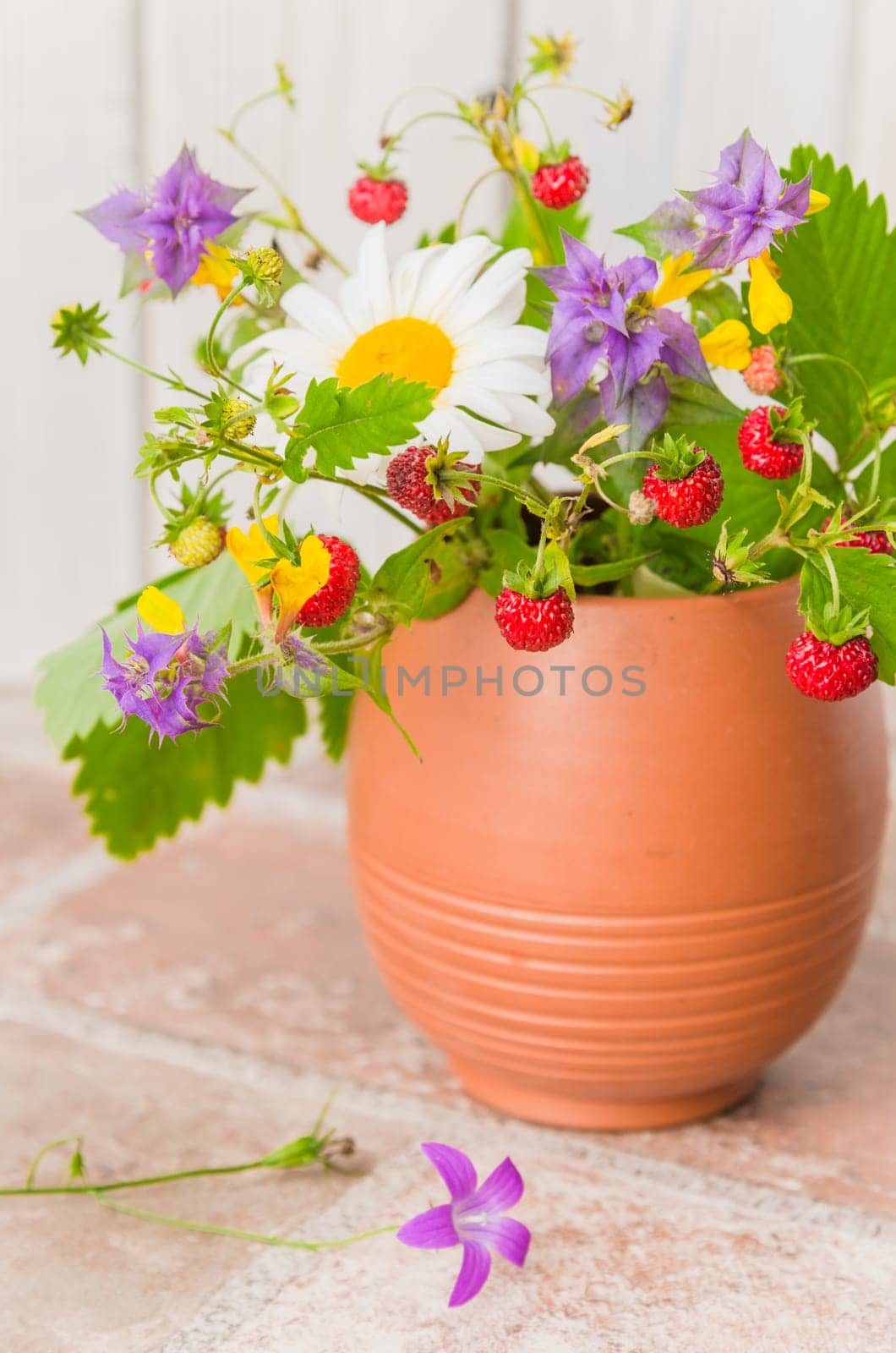 Ripe strawberries and a bouquet of forest flowers in a clay mug