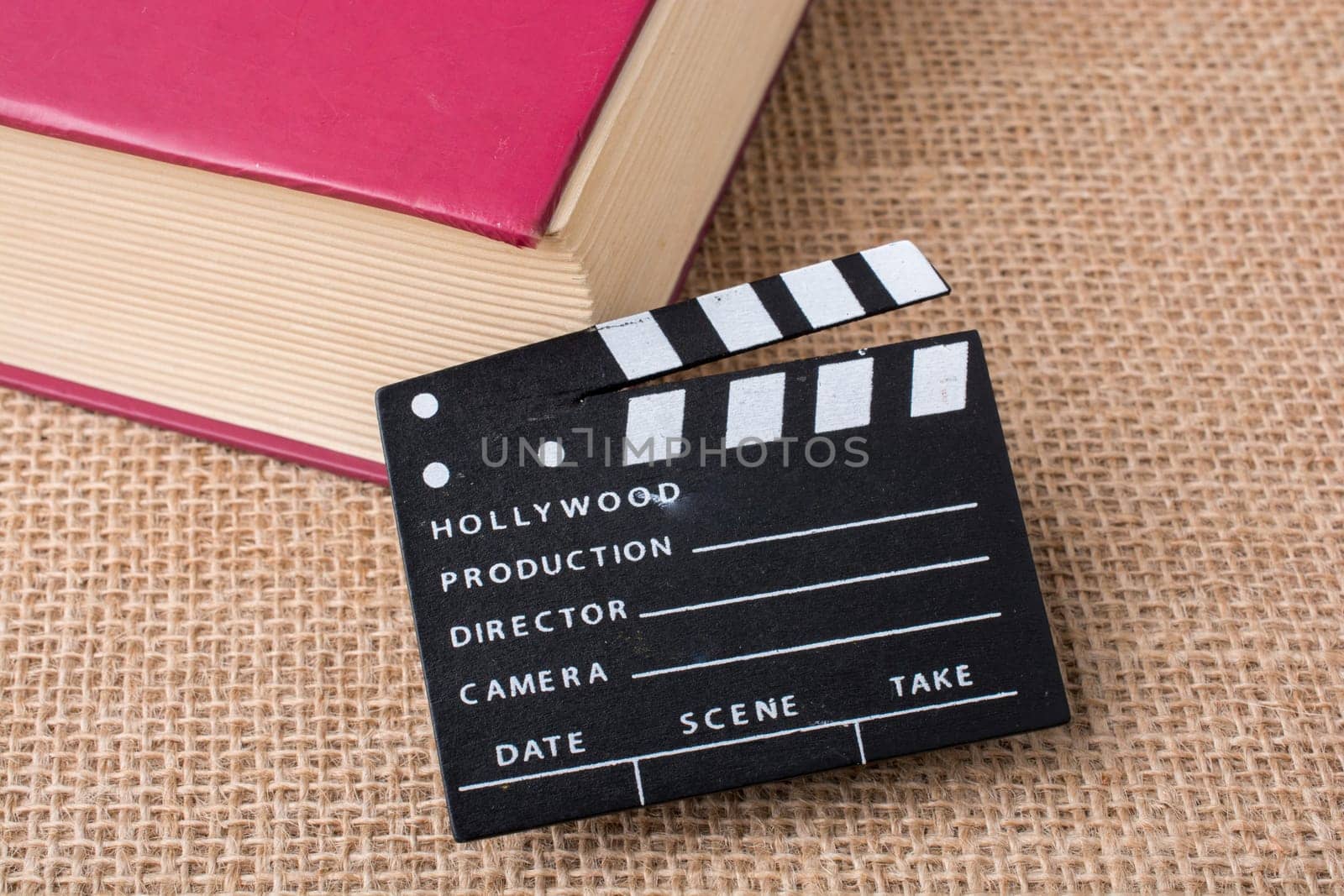 Movie clapper beside a book on a canvas background