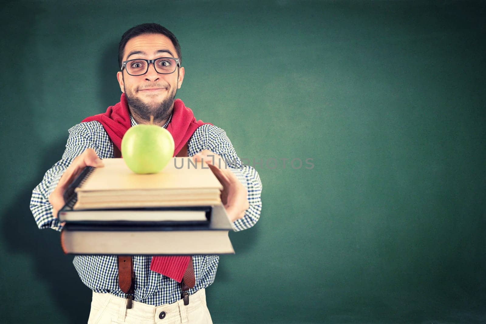 Nerd student posing with books and apple against a chalk board