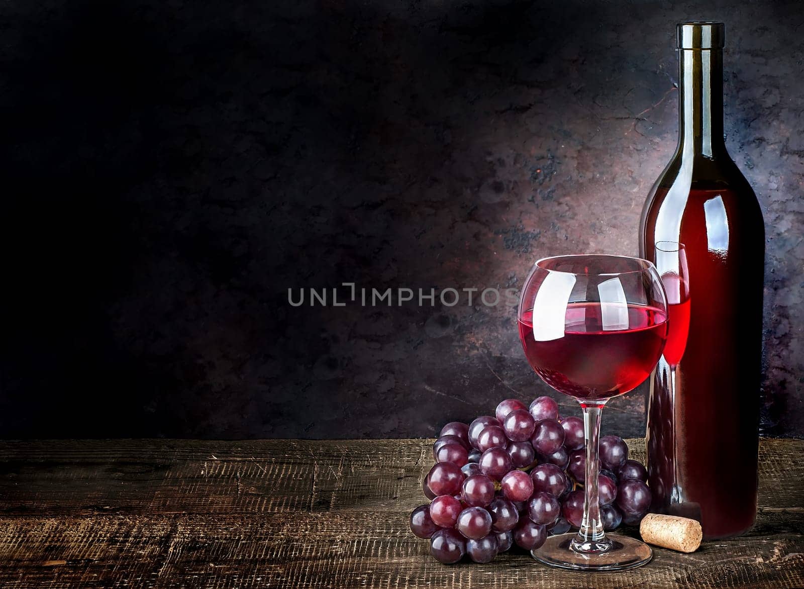 Glass of red wine with grapes and bottle on a wooden table