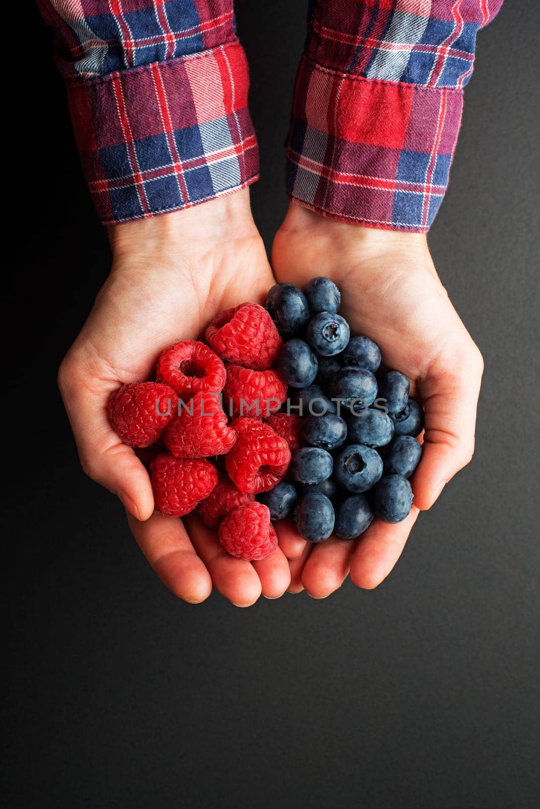 Woman hands holding fresh berries, raspberries and blueberries on black background