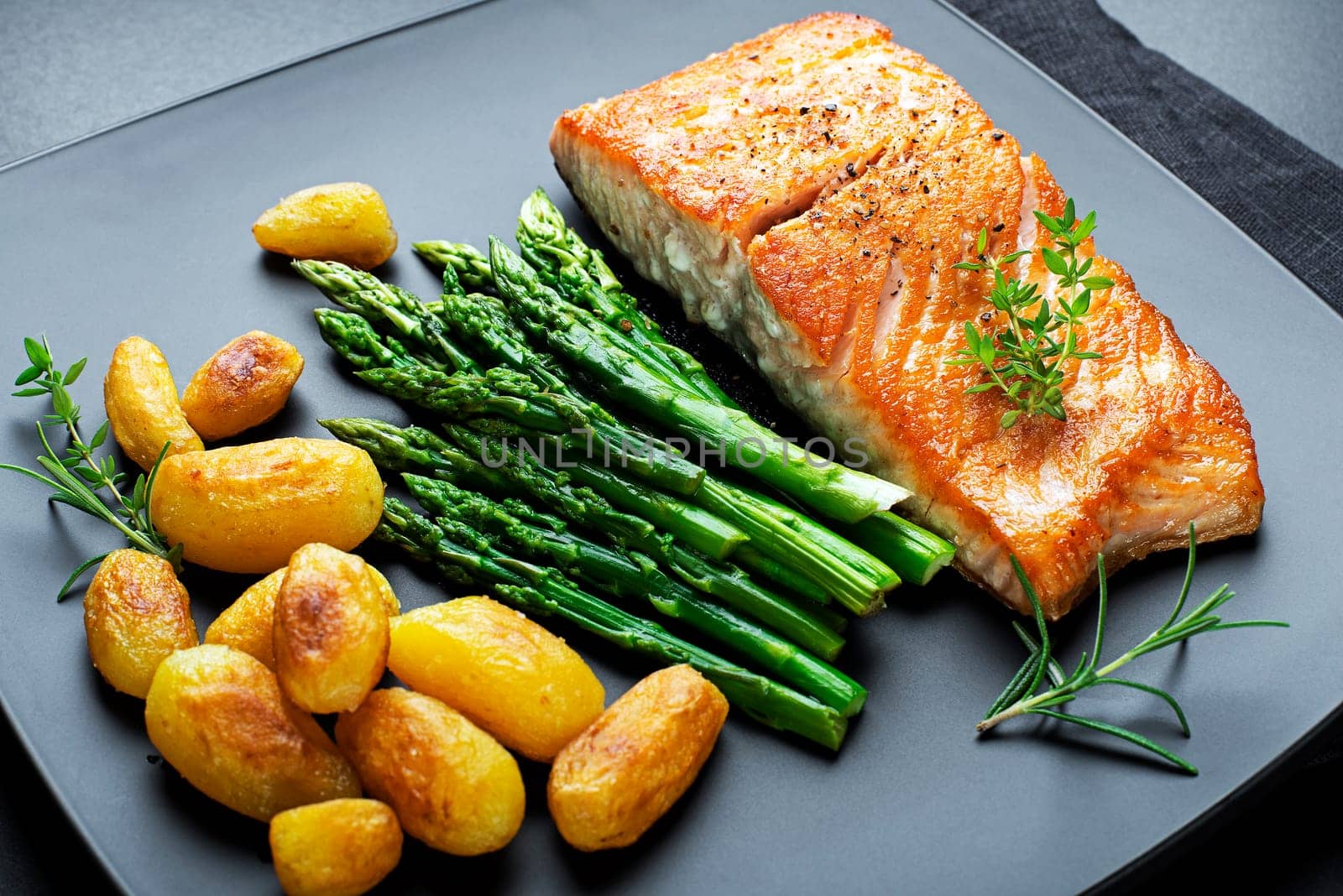 Roasted salmon fillet with asparagus and potatoes on black background