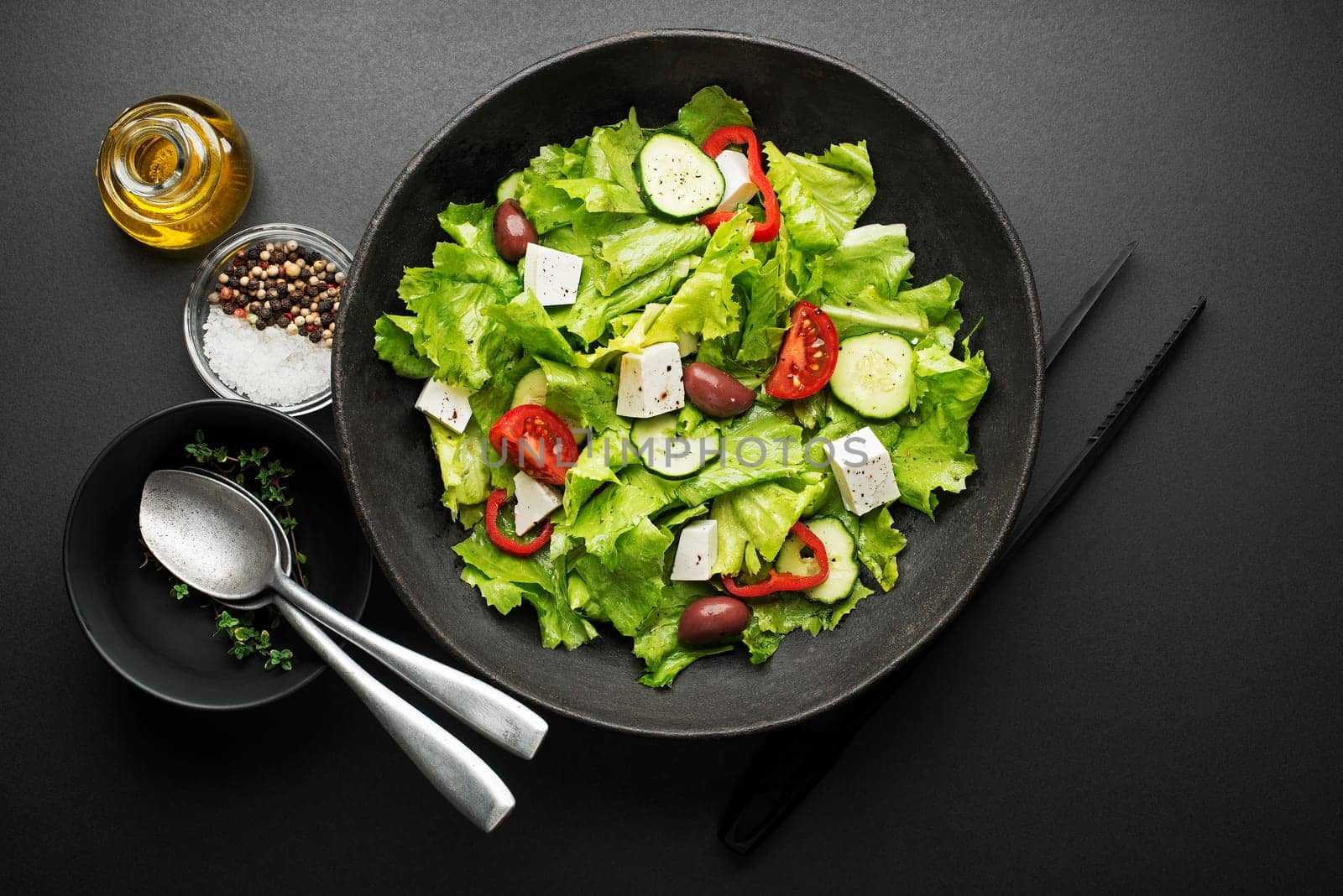 Green salad with cheese and fresh vegetables on a black background. Greek salad.