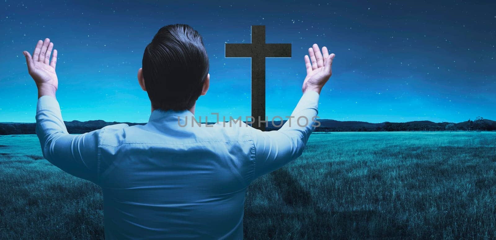 Back view of man raising hand while praying to god over night background