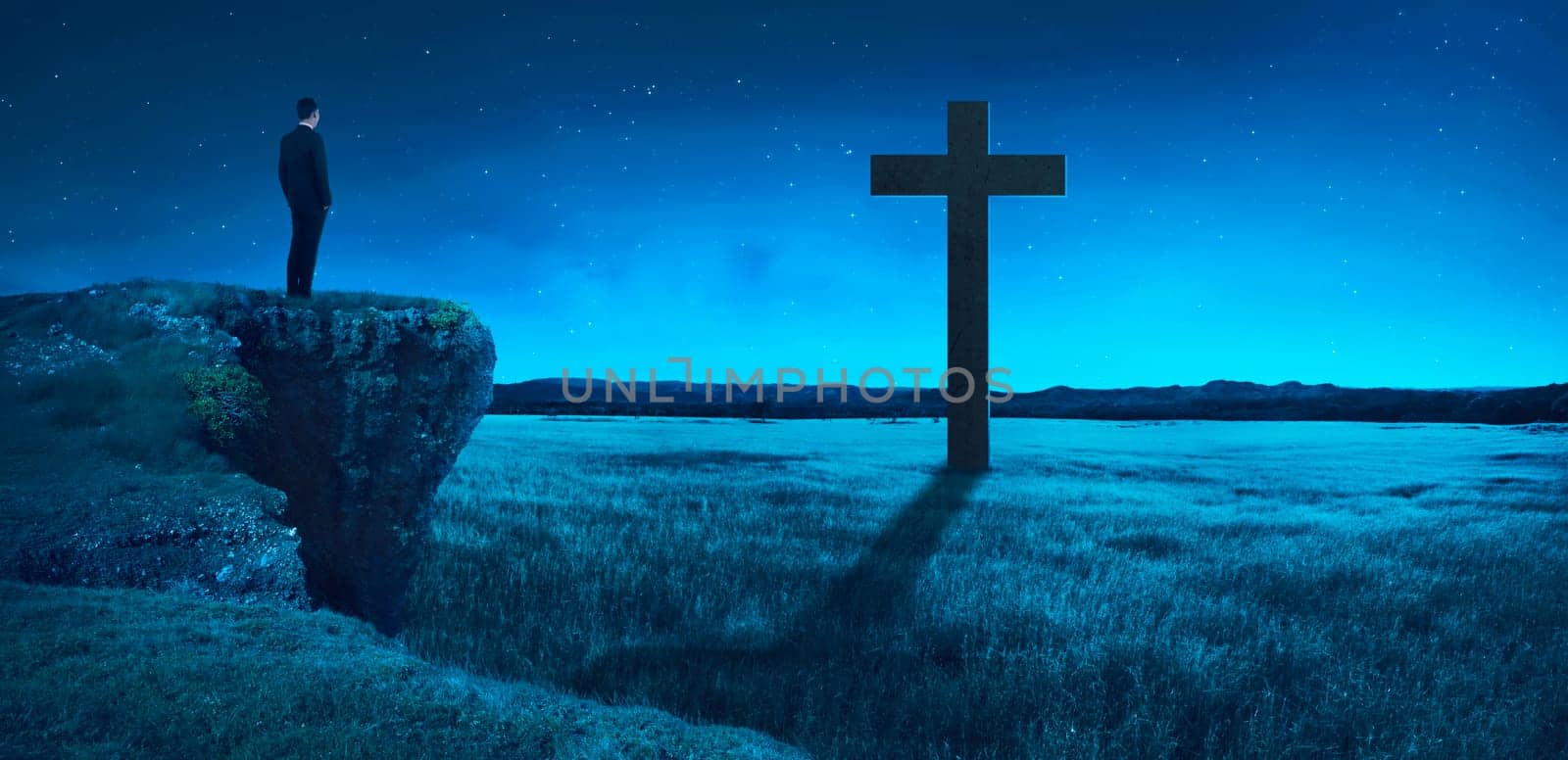 Man standing on the top of the cliff looking to the cross. Religion concept