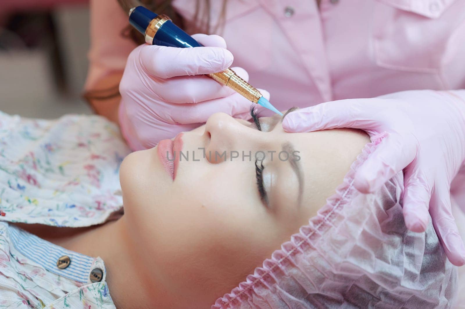 A young woman lies and gets a make-up of her eyebrows in a beauty salon. The use of permanent makeup on the eyebrows. The master works with the eyebrows. Semi-permanent makeup.