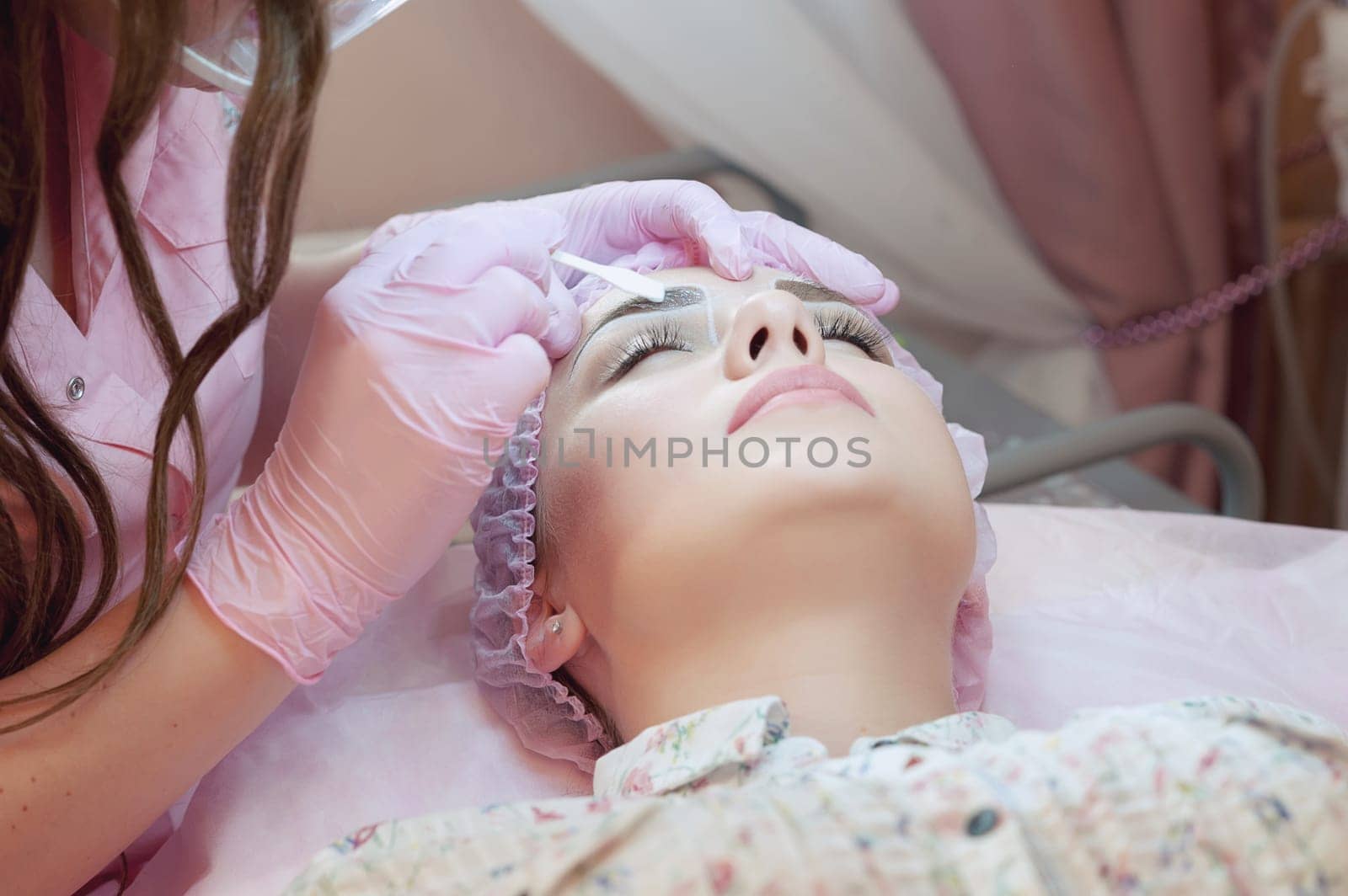 A young woman lies and gets a make-up of her eyebrows in a beauty salon. The use of permanent makeup on the eyebrows. The master works with the eyebrows. Semi-permanent makeup.