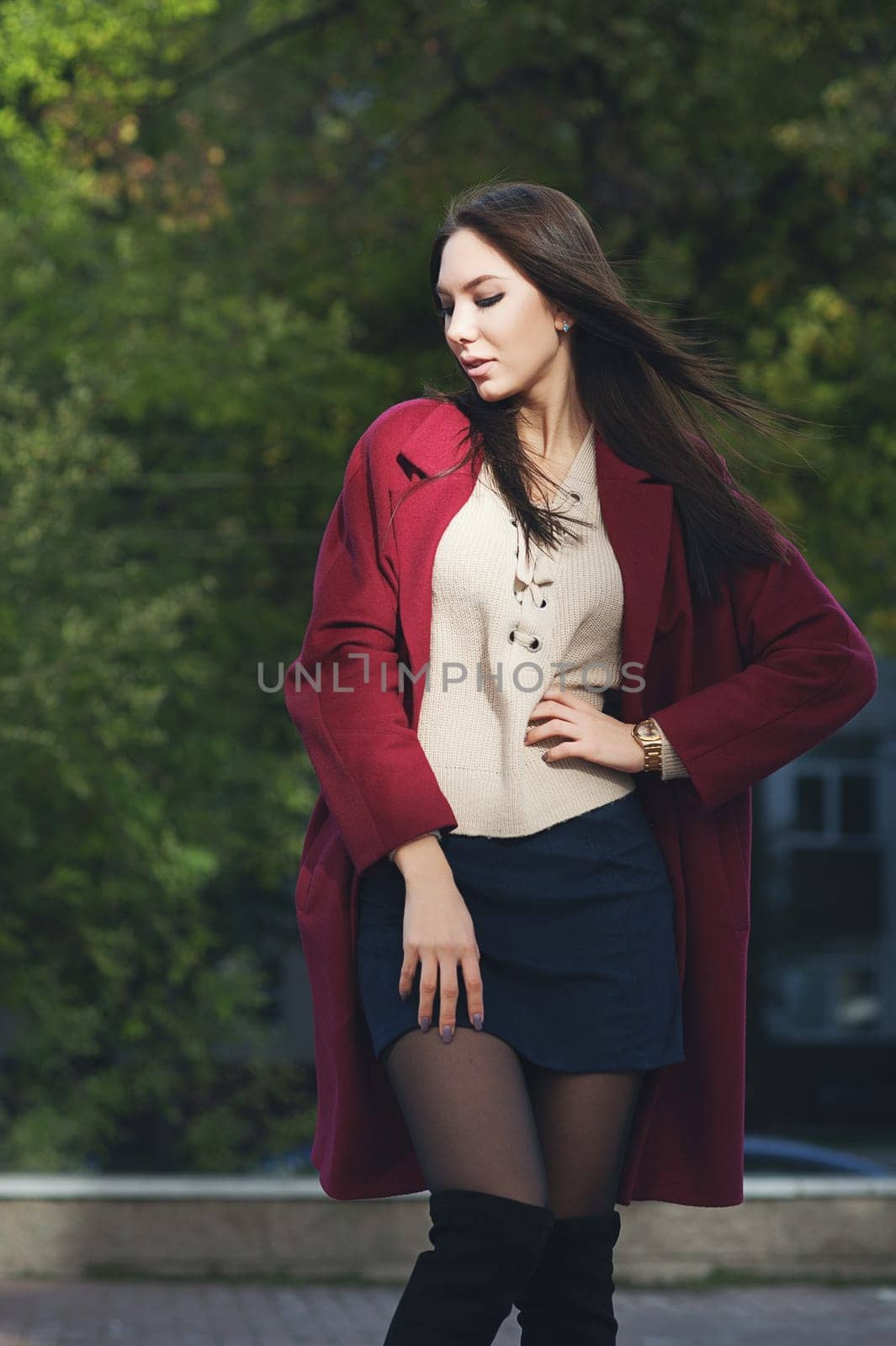 young beautiful stylish woman in claret coat, street style, spring summer trend, dark skirt, beige sweater, flirty.