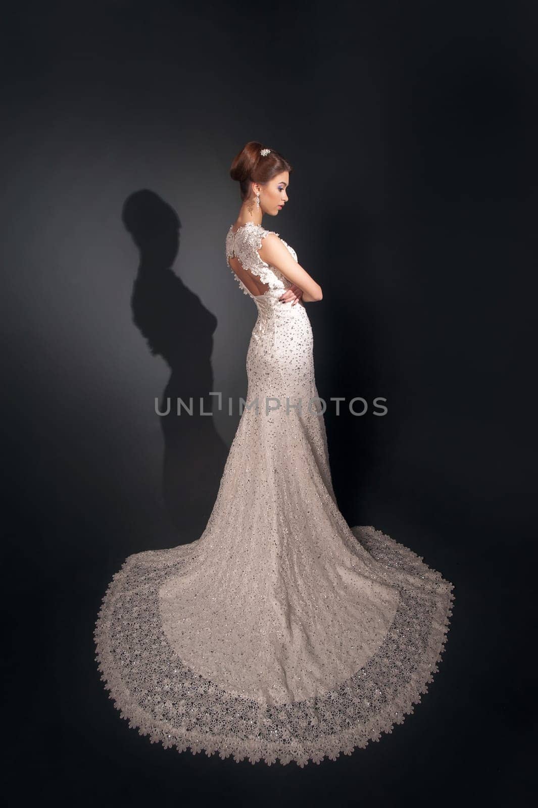Beautiful young bride with makeup and fancy hairstyle in fancy dress sitting on bed.