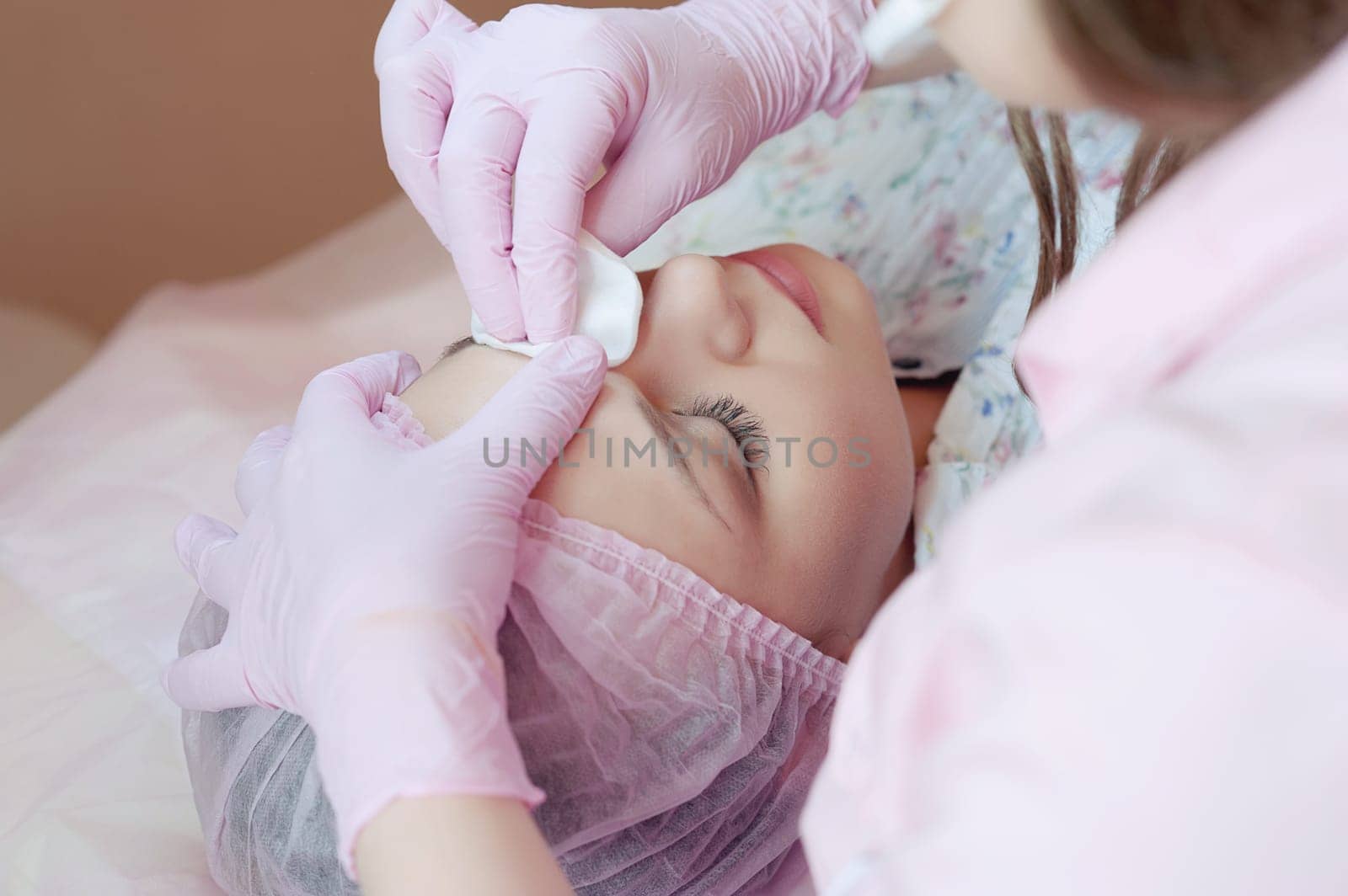 A young woman lies and gets a make-up of her eyebrows in a beauty salon. The use of permanent makeup on the eyebrows. The master works with the eyebrows. Semi-permanent makeup.