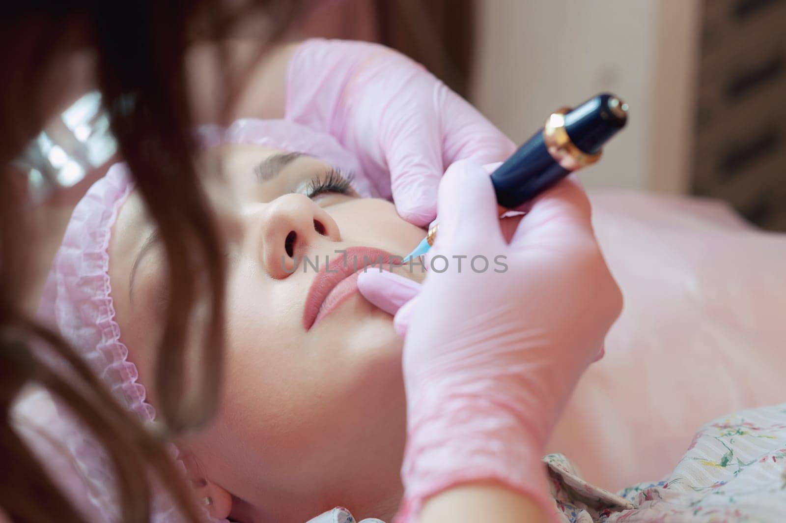 A young woman lies and gets a make-up of her eyebrows in a beauty salon. The use of permanent makeup on the eyebrows. The master works with the eyebrows. Semi-permanent makeup.