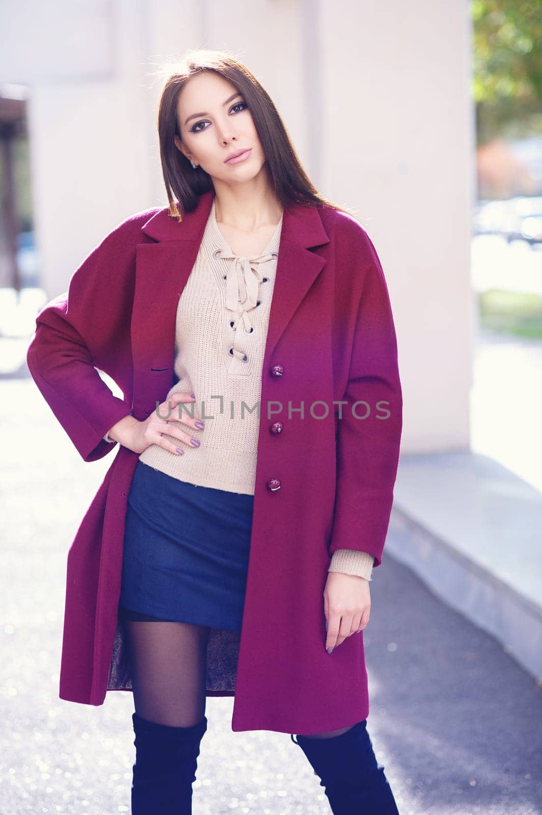 young beautiful stylish woman walking in burgundy coat, street style, spring summer trend, dark skirt, beige jacket, flirty.