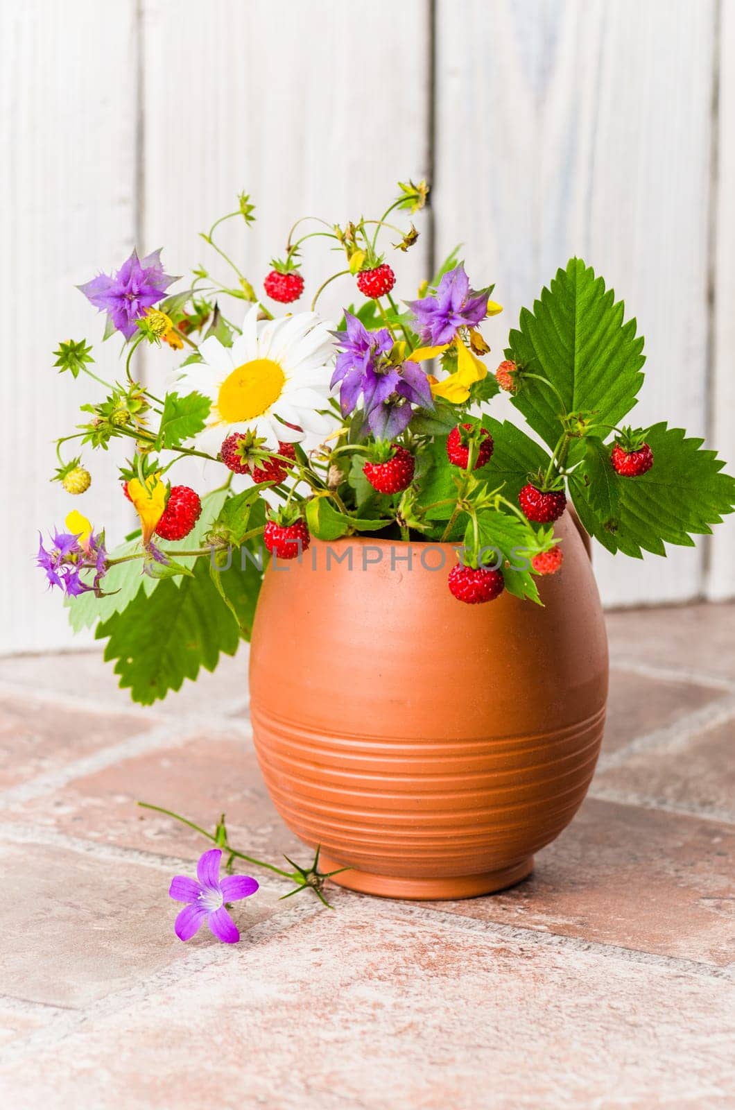 Ripe strawberries and a bouquet of forest flowers in a clay mug