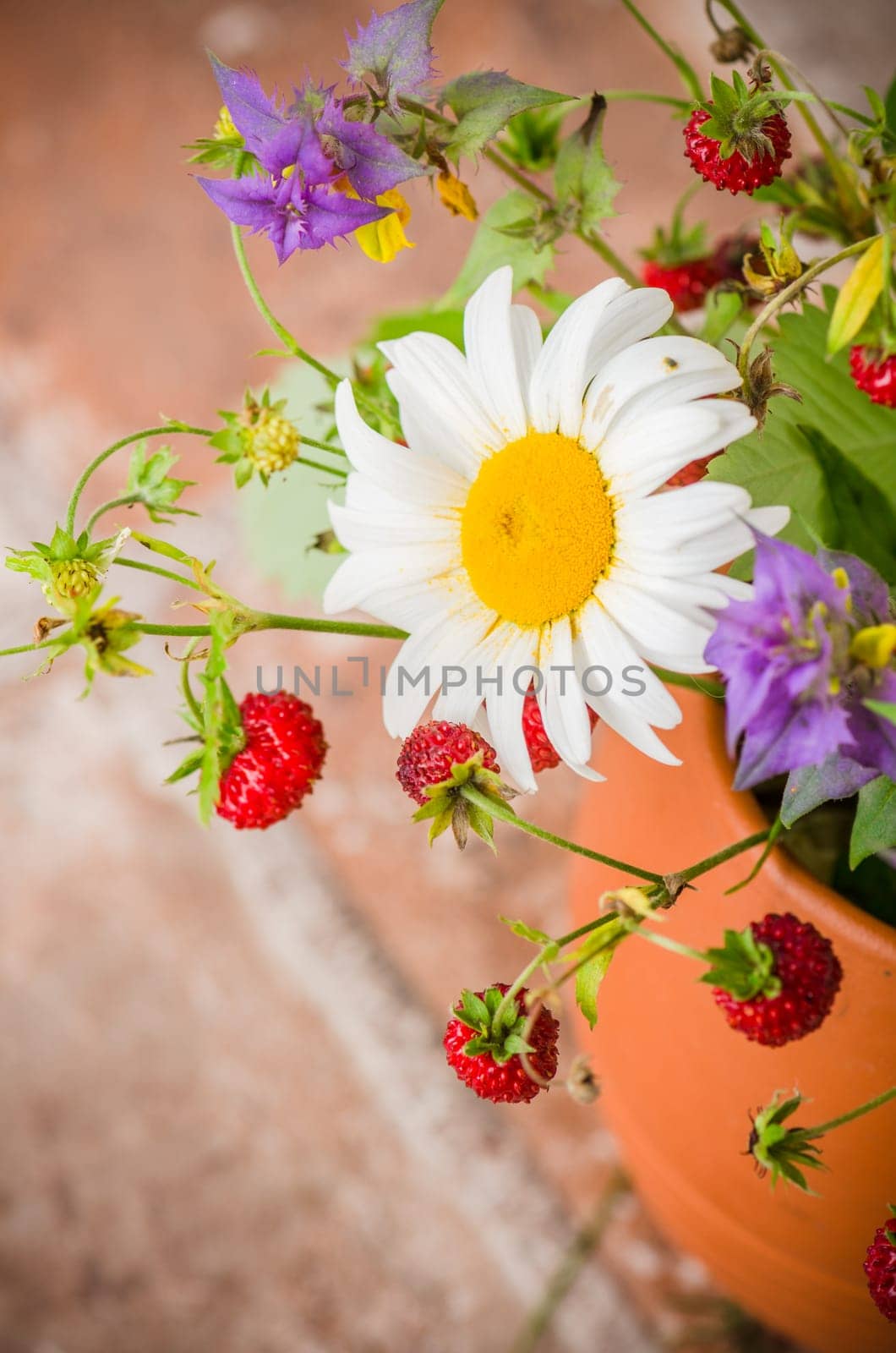 Ripe strawberries and a bouquet of forest flowers in a clay mug