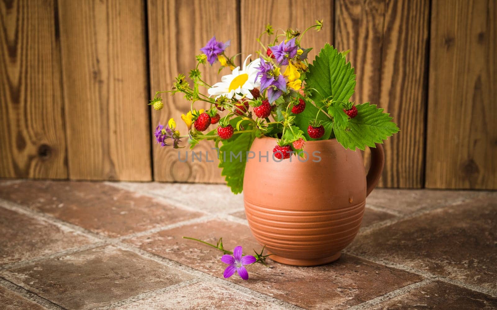Ripe strawberries and a bouquet of forest flowers in a clay mug