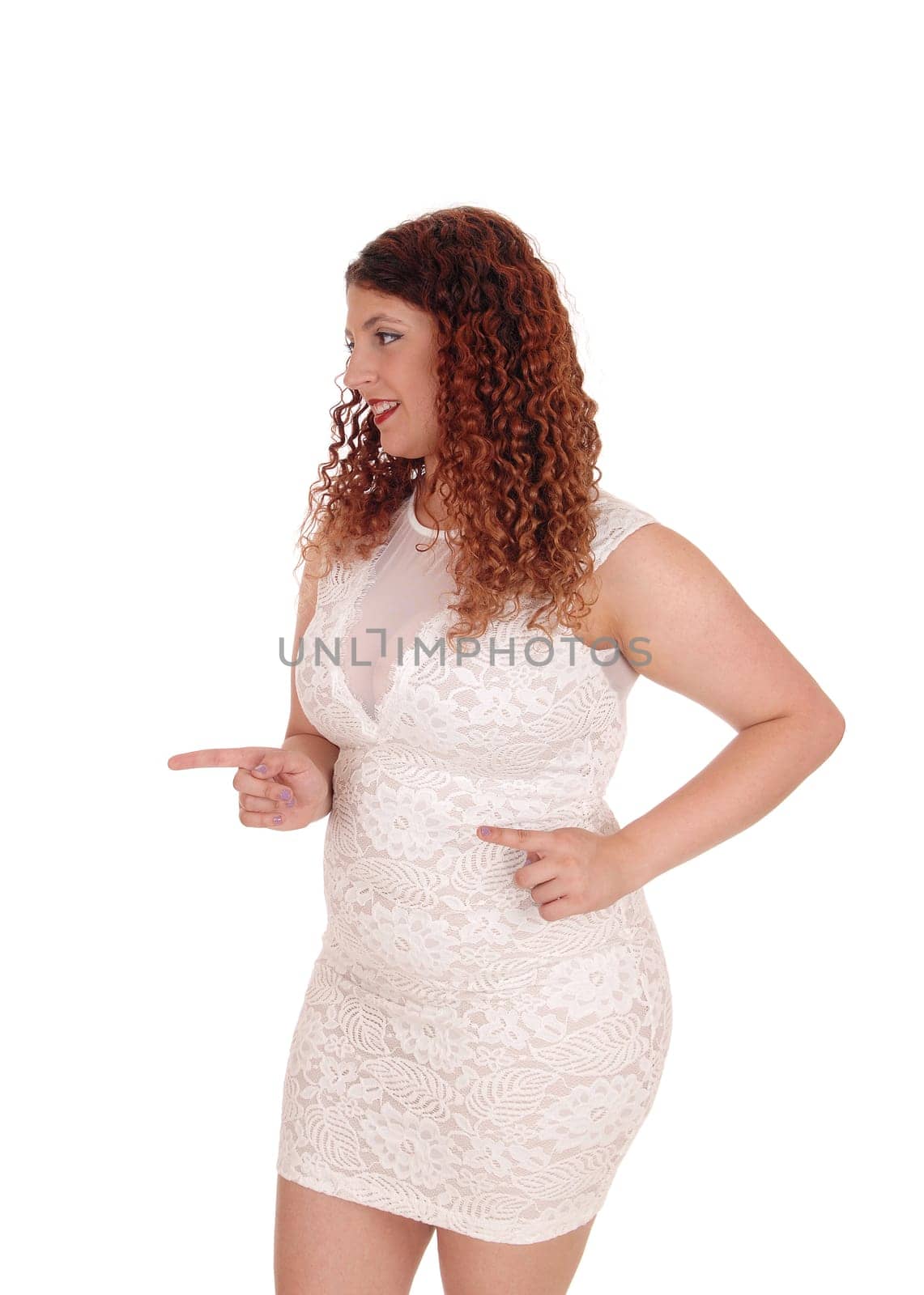 A young beautiful woman in a short dress standing in profile and.pointing with her both of her fingers, isolated for white background.