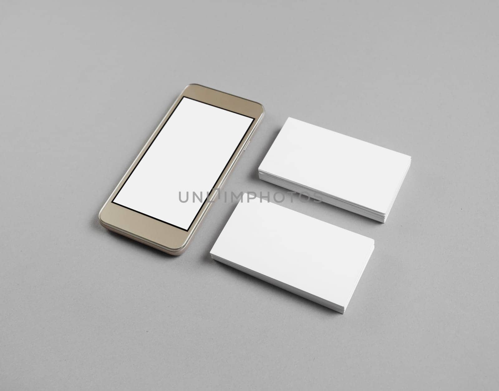 Smartphone with blank screen and two piles of business cards on gray paper background.