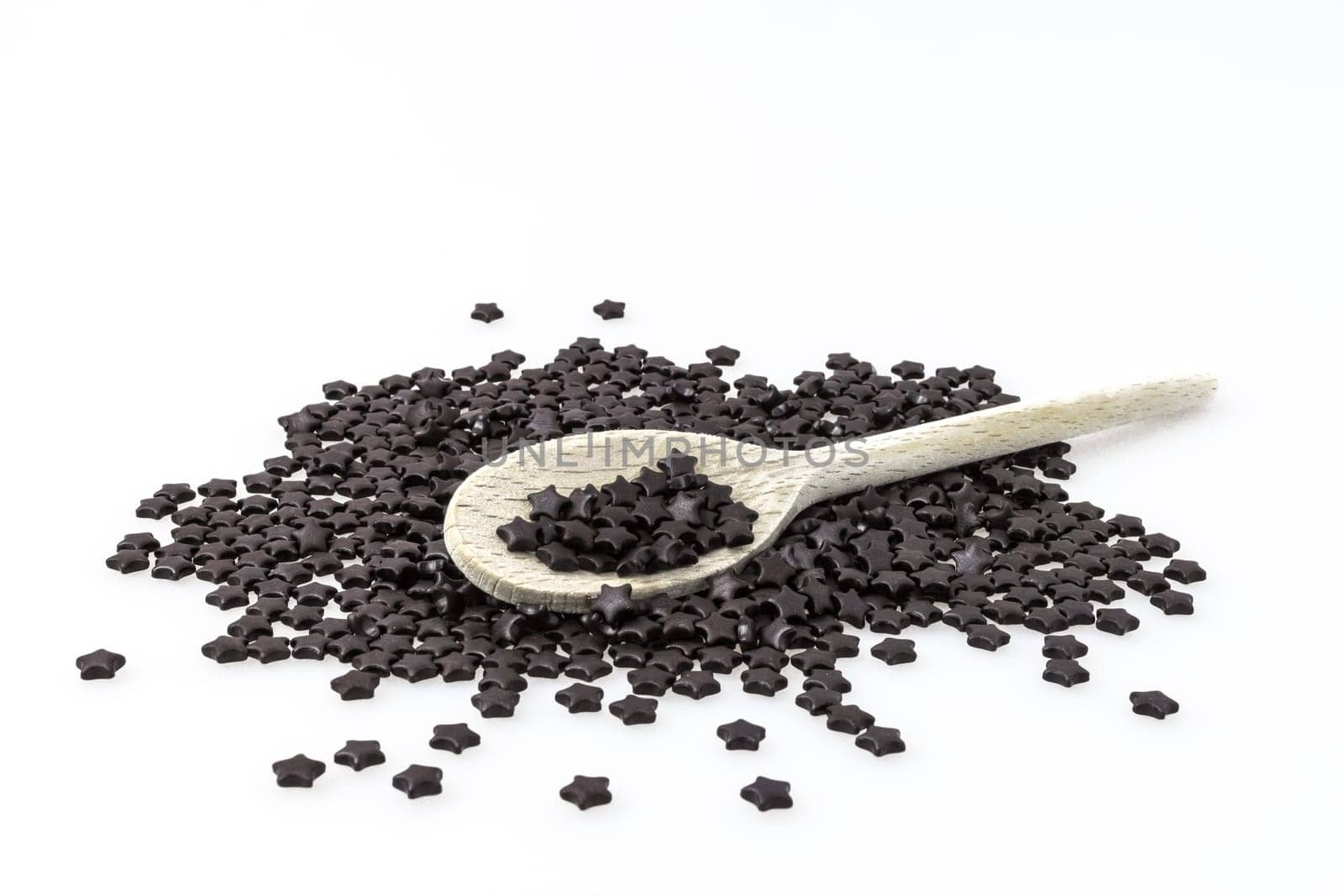 Black liquorice to star shape on white background. In the middle, a wooden spoon.