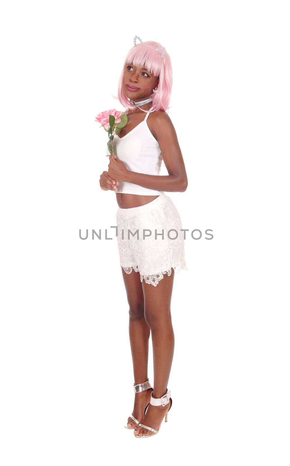A beautiful African woman in white shorts, holding a pink rose with.pink hair standing in profile over white background.
