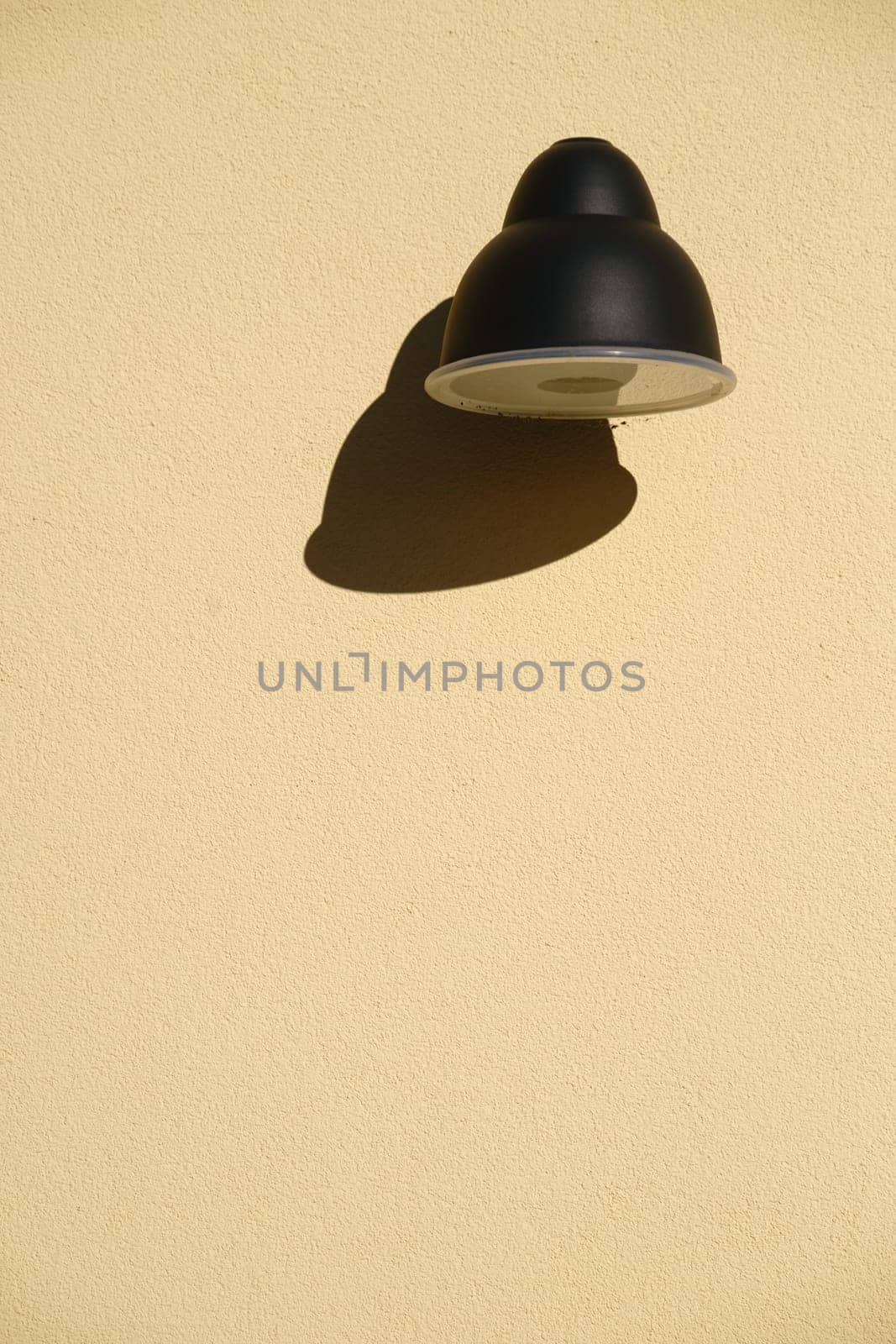 The close-up of a wall lamp that casts a shadow on a plaster façade.