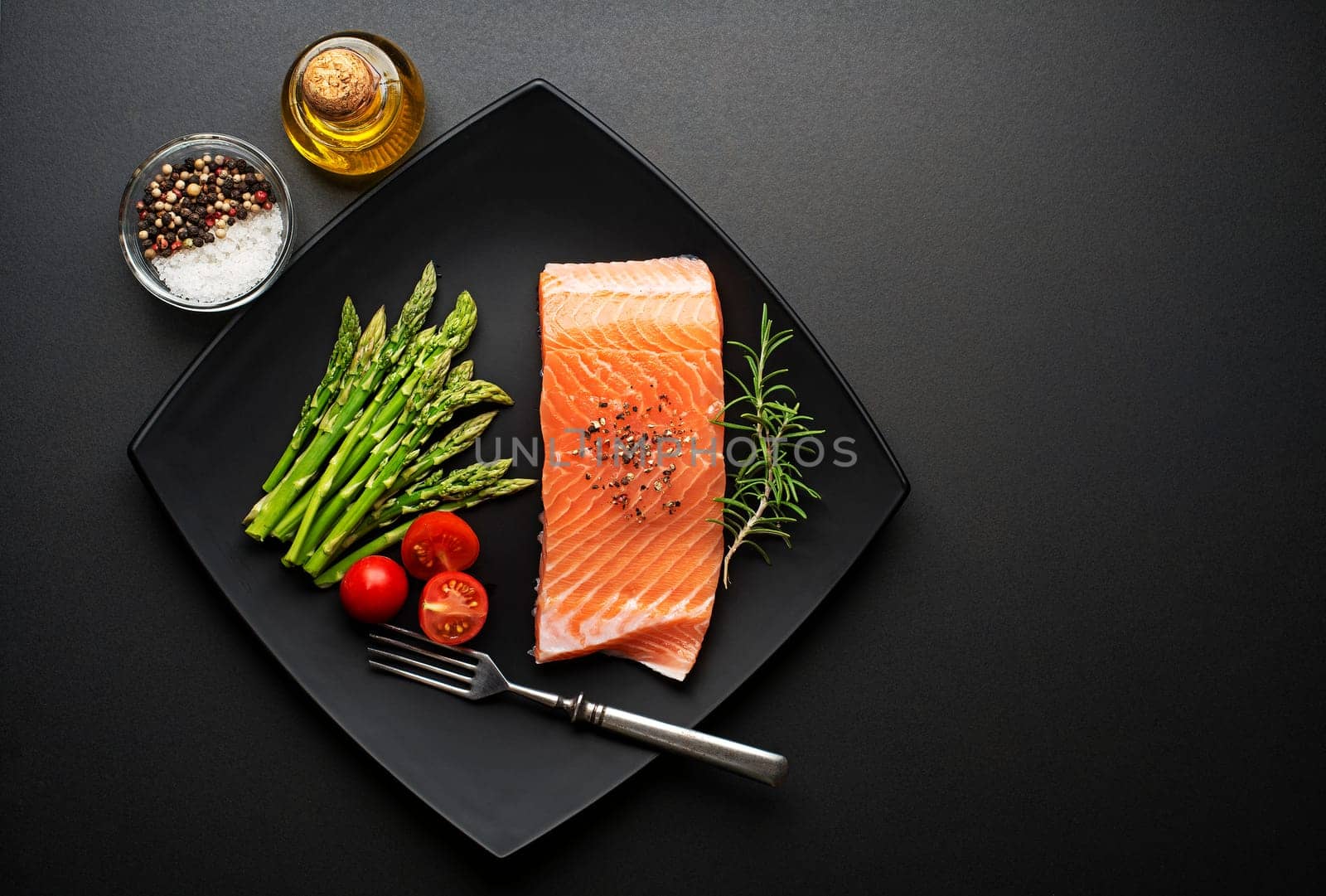 Raw steak of salmon with fresh ingredients on black background