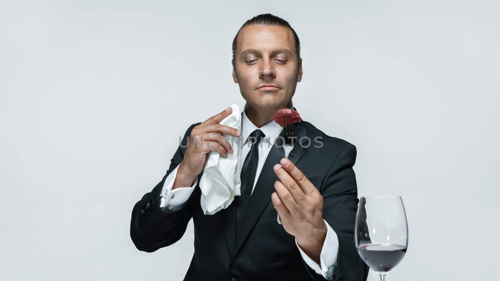 Portrait of a young man in image of maniak with knife, fork and and a piece of raw meat on a plate. Man in suit. The image in the style of Halloween