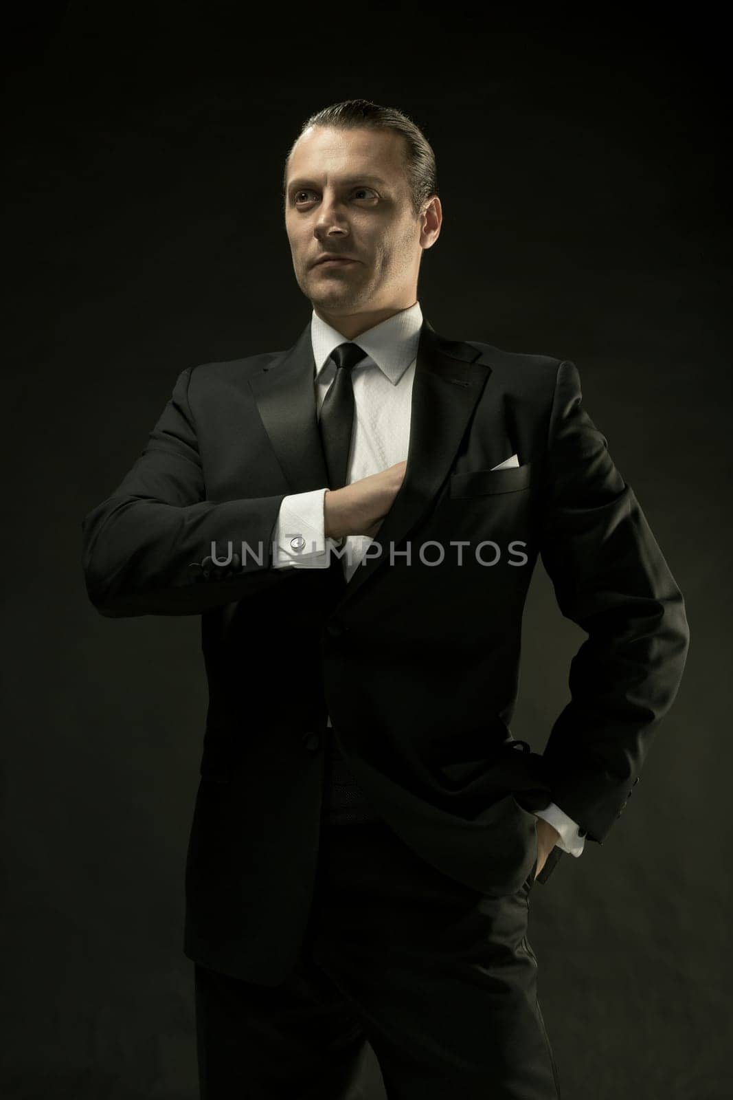 The attractive mature man in black suit on dark studio background