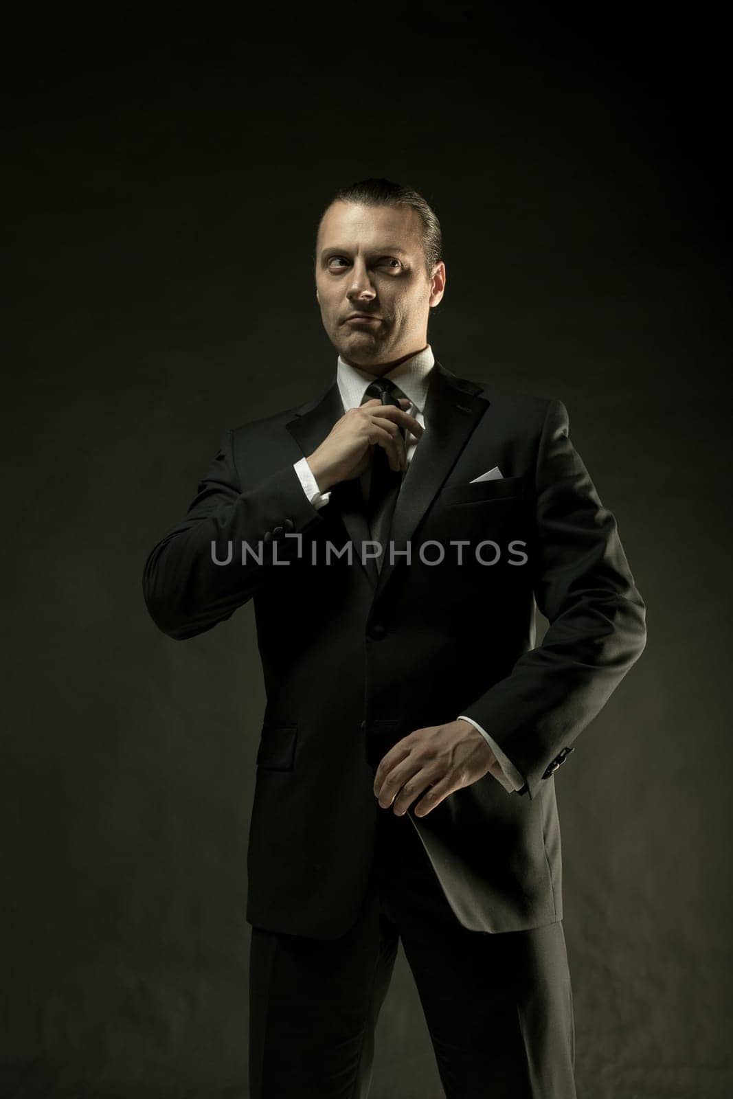 The attractive mature man in black suit on dark studio background