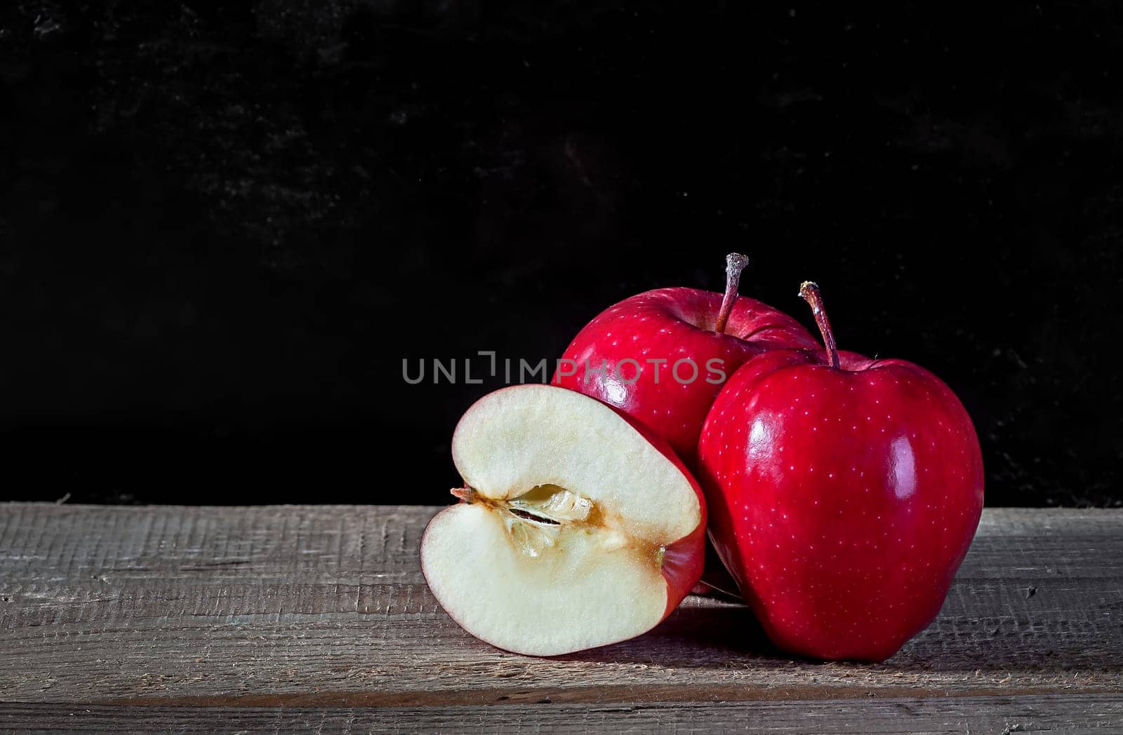 Whole and cut in half apple lying on textured wooden table on dark background