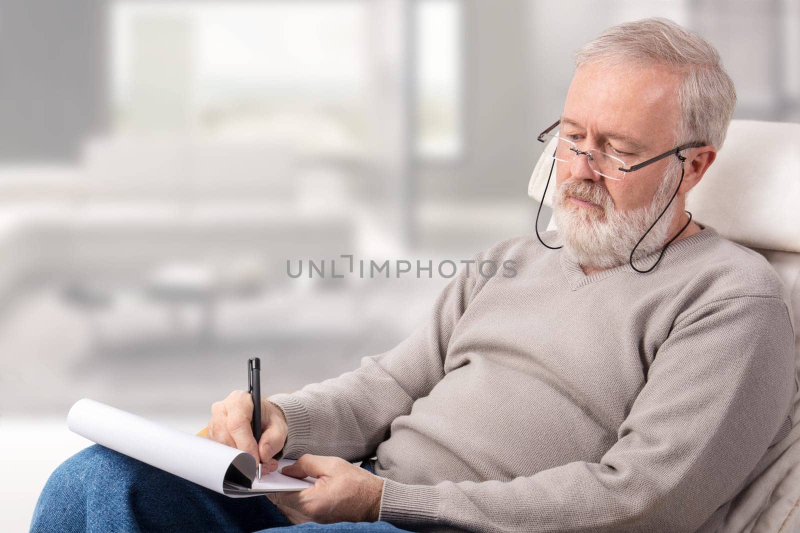 Old man making a shopping list with a pen on paper for holidays