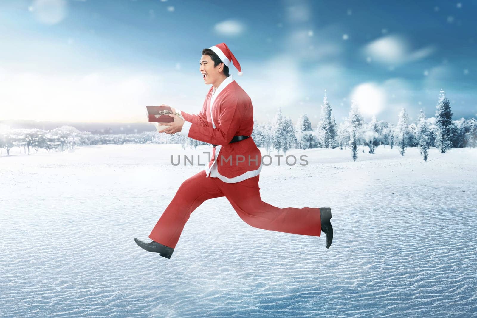 Happy asian man wearing santa claus costume with xmas gift on snowy field background
