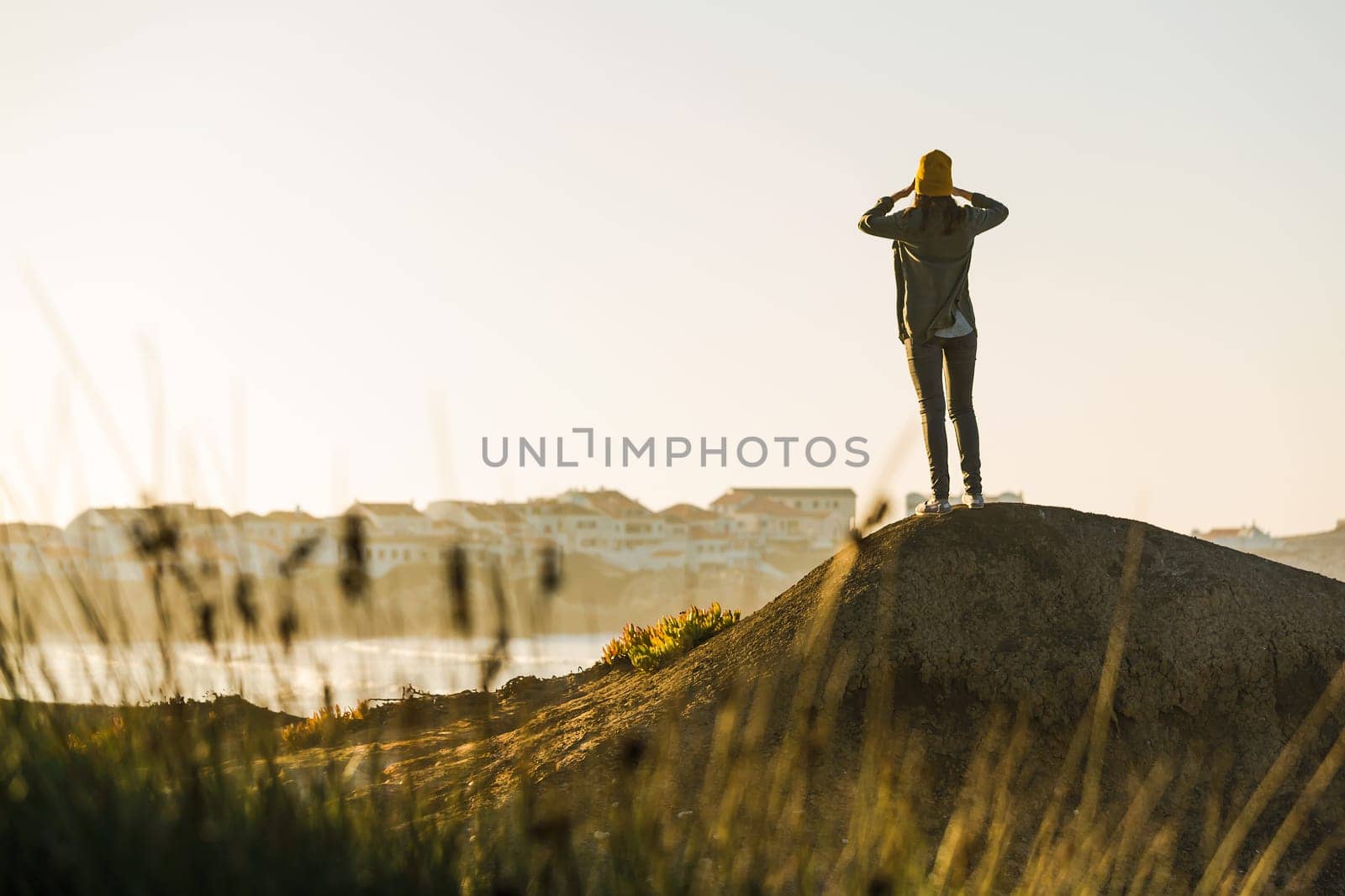 Beautiful woman with yellow cap over the cliff seeing the beach