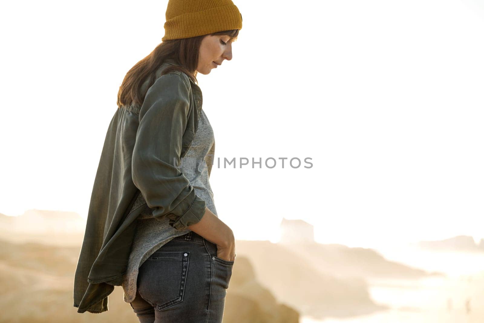 Beautiful woman with yellow cap over the cliff seeing the beach