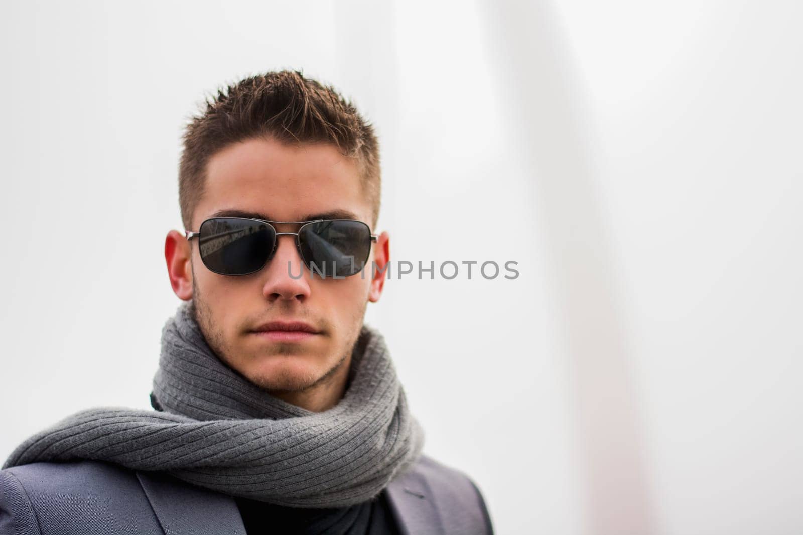 Headshot of attractive young man outdoor wearing sunglasses and scarf on elegant jacket