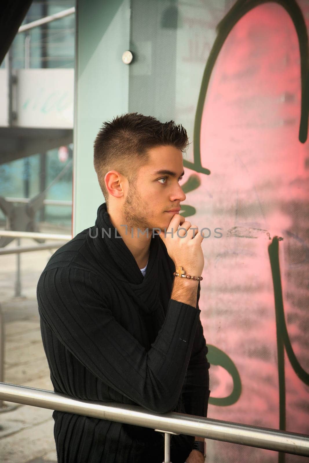 Handsome young man outdoor in city setting, wearing winter clothes, side view