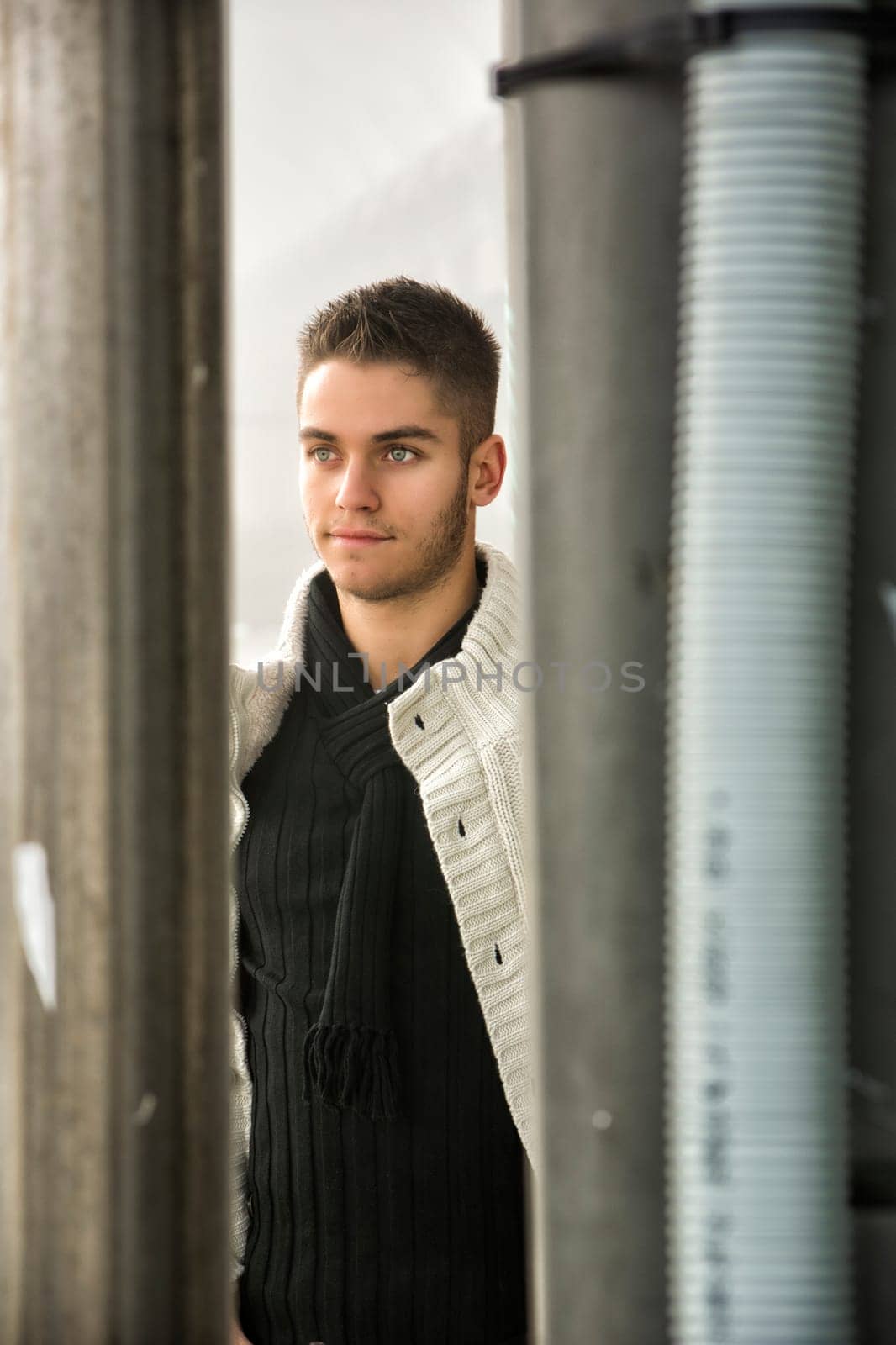 Happy young man outdoor seen between two pillars. Wearing winter clothes