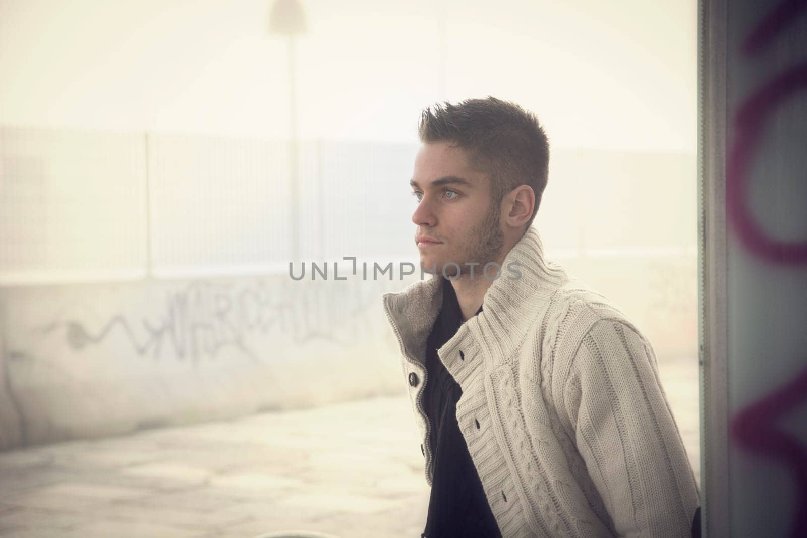 Handsome young man outdoor in city setting, wearing winter clothes, side view